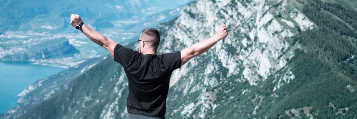 Man standing with arms raised in celebration overlooking a breathtaking mountain landscape.